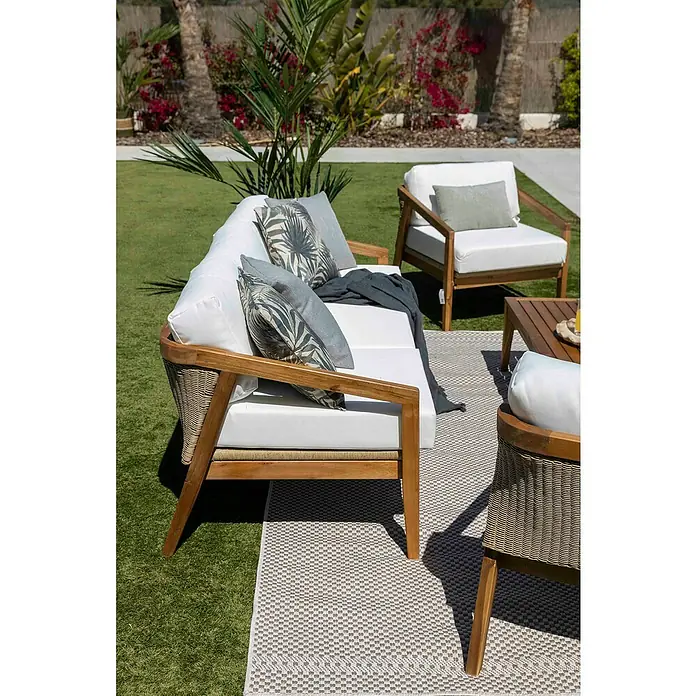 Sunfun Conjunto de muebles Anna - 4 pzs., Madera de acacia, Marrón - Un elegante patio con un juego de sofás de ratán y un sillón a juego sobre una alfombra de exterior estampada.