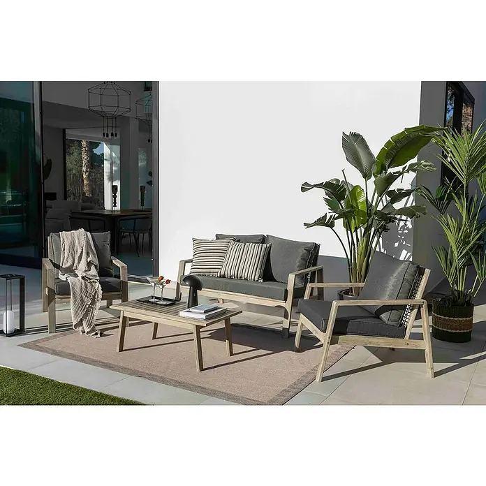 Sunfun Conjunto de muebles Chenoa - 4 pzs., Madera de acacia, Marrón - Un moderno conjunto de patio con un sofá gris, sillón, mesa y alfombra en un patio con plantas, que invita a la relajación.