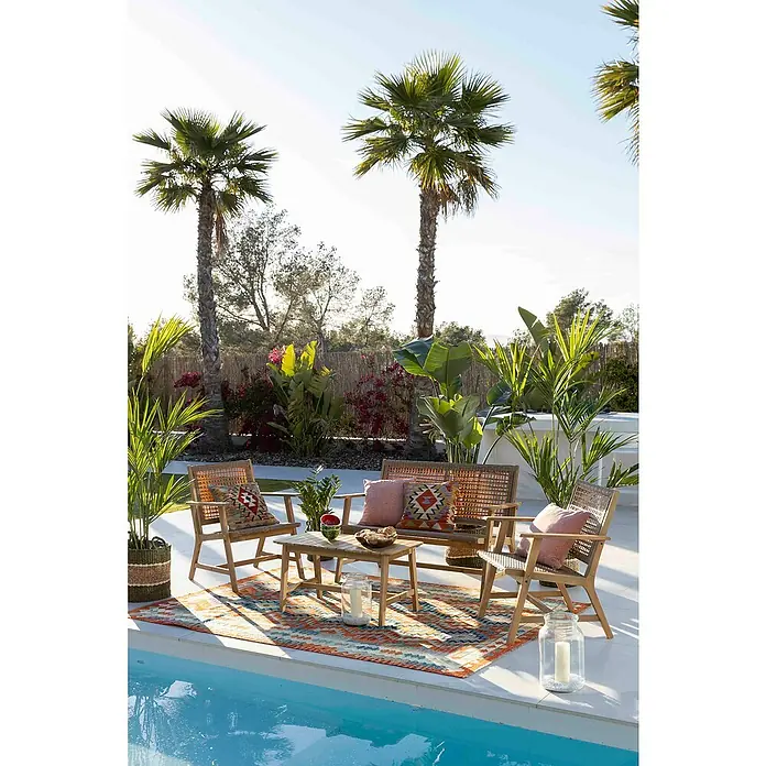 Conjunto de muebles Violeta - 4 pzs., Madera de acacia/Ratán sintético, Marrón - Una acogedora escena de salón al aire libre con muebles de ratán y cojines coloridos junto a una piscina, rodeada de exuberantes palmeras.