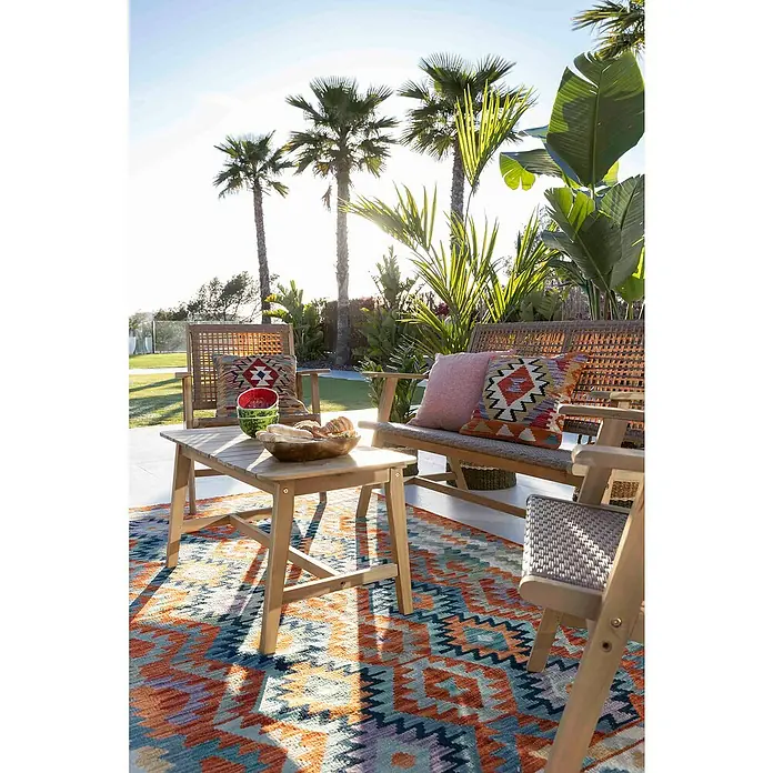 Conjunto de muebles Violeta - 4 pzs., Madera de acacia/Ratán sintético, Marrón - Juego de muebles de jardín con mesa de madera de acacia, sofá de ratán y sillas sobre una alfombra estampada con vegetación tropical de fondo.