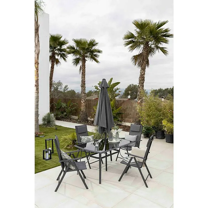 Set de muebles de jardín Donavan - 6 pzs., Antracita, Incluye Parasol - Un conjunto de patio con mesa, sillas y sombrilla, situado en un patio con baldosas y rodeado de palmeras y vegetación.