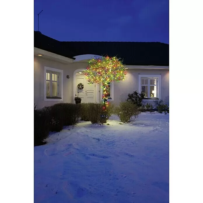 Konstsmide LED-Lichterkette Micro LED - Außen, Lichtfarbe: Mehrfarbig, Anzahl Leuchtmittel: 40 Stk., Netzbetrieben - Bunter Lichterbaum vor einem verschneiten Haus bei Abenddämmerung.
