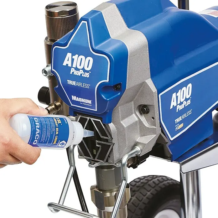 Lubricante - 250 ml, Específico para: Graco Magnum Sistema de pulverización A 100 - Un primer plano del pulverizador de pintura airless Graco A100 ProPlus con una mano que añade líquido lubricante.