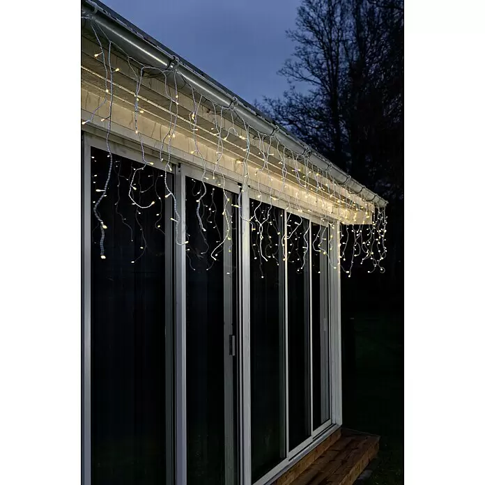 Konstsmide LED-Lichtervorhang Eisregen - Außen, 0,9 m, Bernstein, 96 Stk., Netzbetrieben - Warmweiße LED-Eiszapfenlichter mit weißen Kabeln schmücken die Traufe eines modernen Gebäudes in der Dämmerung.