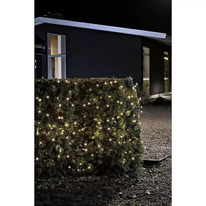 Konstsmide LED-Lichterkette - Außen, Lichtfarbe: Bernstein, 1,9 m - Warme weiße LED-Lichterkette beleuchtet eine dunkelgrüne Hecke bei Nacht, im Hintergrund ein modernes Haus.