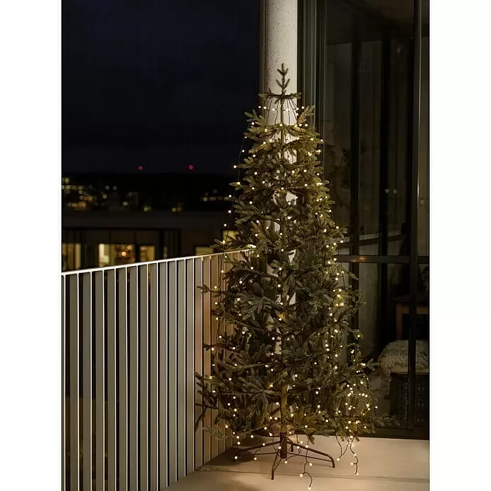 Konstsmide LED-Lichterkette Baummantel - Außen, Lichtfarbe: Bernstein, Anzahl Leuchtmittel: 240 Stk., Netzbetrieben, 12,4 m - Künstlicher Weihnachtsbaum mit warmweißen Lichterketten auf einem Balkon bei Nacht, schafft festliche Außenstimmung.