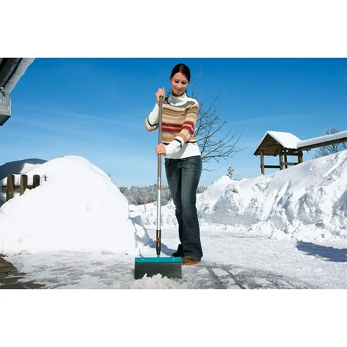 Gardena Combisystem Holzstiel - 130 cm - Frau benutzt einen Gardena Eiskratzer mit Stiel, um eine vereiste Fläche freizumachen, mit Schnee im Hintergrund.