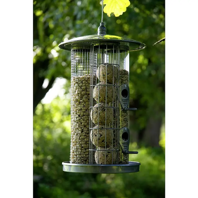 Dobar Futterspender - L x B x H: 21,5 x 21,5 x 36,5 cm, Metall, 3 Futterkammern - Nahaufnahme eines mit Futter, Fettkugeln und Erdnüssen gefüllten Vogelfutterhäuschens, das an einem Baum hängt und Vögel anlockt.