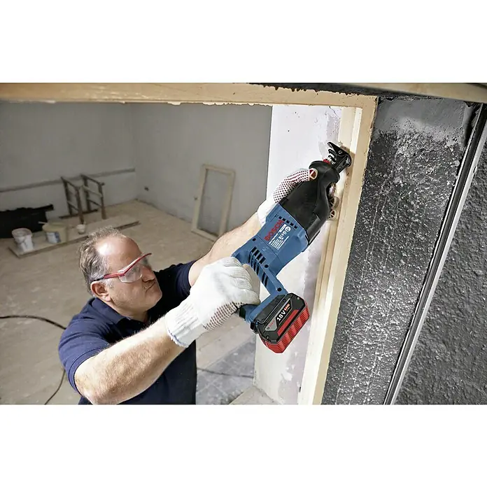 Bosch Professional AMPShare 18V Akku-Säbelsäge GSA 18 V-LI - 18 V, Ohne Akku, Leerlaufhubzahl: 0 /min - 2.700 /min - Ein Mann mit Schutzbrille benutzt eine Bosch Akku-Säbelsäge, um einen Holzrahmen zu schneiden. Das Werkzeug ist blau und schwarz mit einem roten 18V Akku.