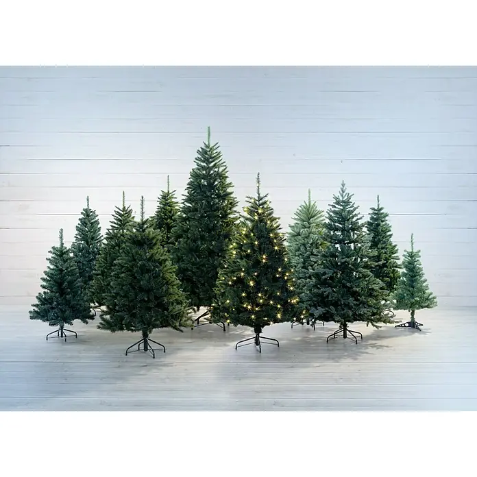Künstlicher Weihnachtsbaum Canmore - Höhe: 185 cm, Grün - Eine Gruppe von künstlichen Weihnachtsbäumen unterschiedlicher Größe, einer davon mit warmweißen Lichtern geschmückt, vor einem weißen Holzhintergrund.