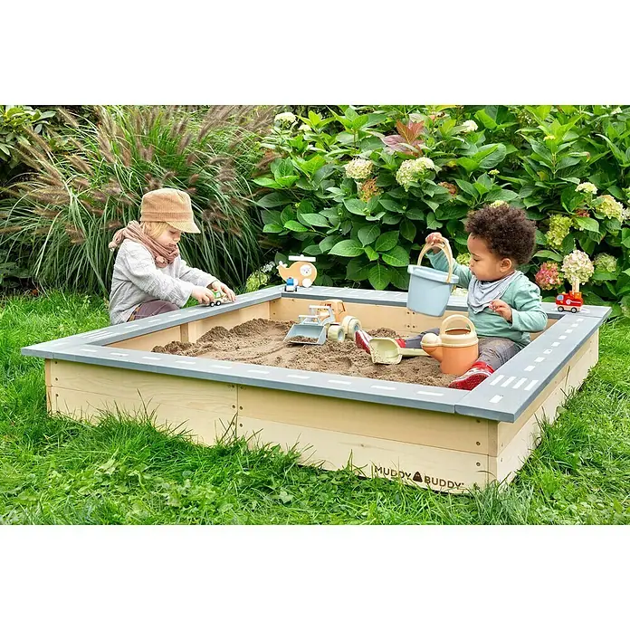Muddy Buddy Sandkasten Highway Hero - L x B x H: 135 x 125 x 20 cm, Holz - Kinder spielen in einem Muddy Buddy Sandkasten mit Spielzeugautos, einem Eimer und einer Gießkanne.