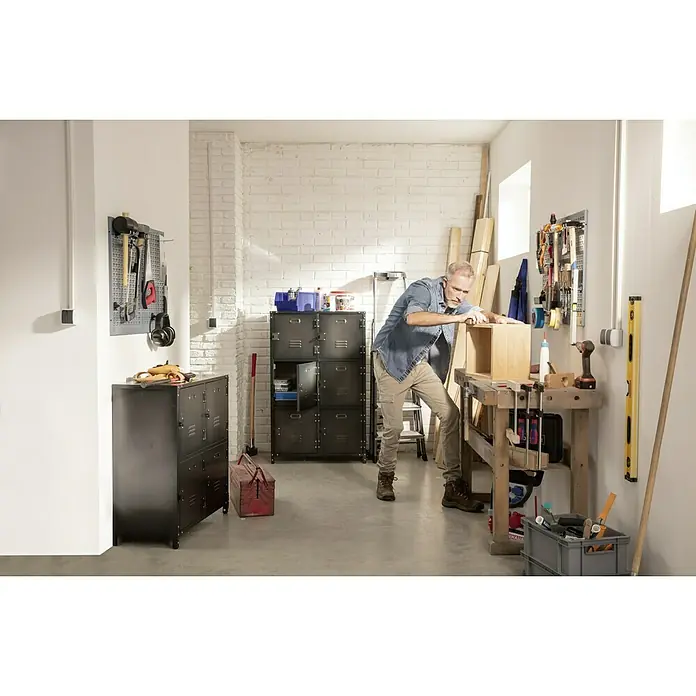 Metall-Mehrzweckschrank Vintage Industrial Style - 35 x 75 x 120 cm, Anzahl Türen: 6 Stk., Anzahl Fächer: 6 Stk. - Werkstatt eines Handwerkers mit Werkbank und Aufbewahrungsschränken, in der ein Mann an einem Holzprojekt arbeitet.