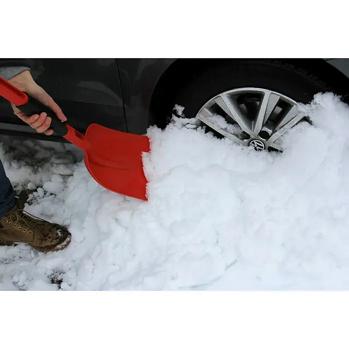 Gardol Klappschaufel - Kunststoff - Eine rote Schneeschaufel räumt Schnee um ein Auto frei, wobei der Fokus auf der Schaufel und ihrer Verwendung liegt.