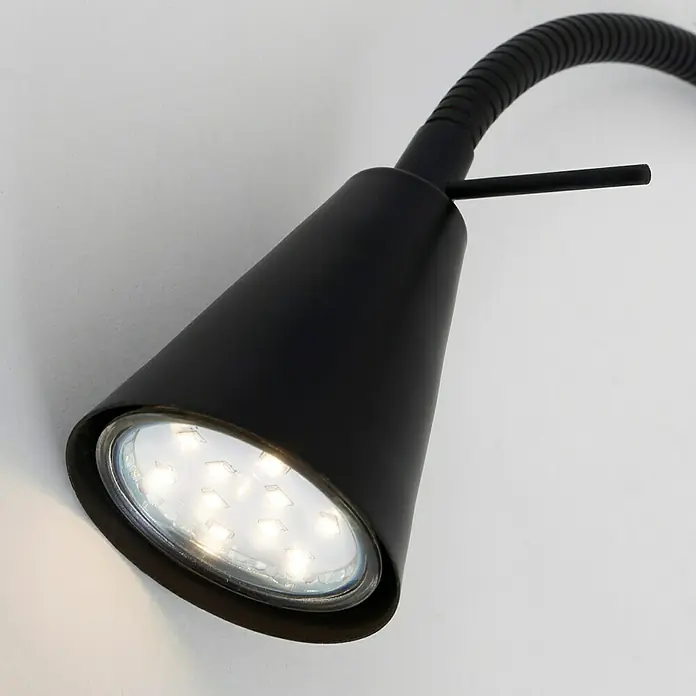 Briloner LED-Wandstrahler Tuso - 4 W, L x B x H: 5,8 x 21,7 x 40,3 cm, Schwarz, Warmweiß - Nahaufnahme einer modernen, schwarzen LED-Wandleuchte mit flexiblem Arm, die Licht auf eine weiße Oberfläche wirft.