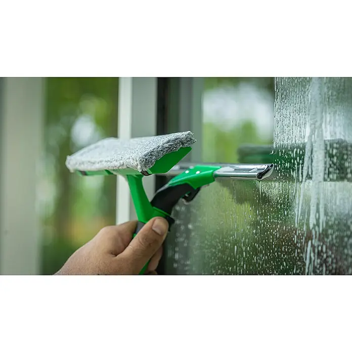 Unger Mikrofaser-Reinigungspad Visa Versa Pro - Breite Bezug: 35 cm, 100 % Polyacryl (Fasern) - Nahaufnahme eines Fensterwischers mit grünem Griff, der eine schmutzige Glasscheibe reinigt. Das Reinigungswerkzeug entfernt Seifenwasser und Schmutz.