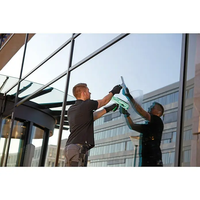 Unger ErgoTec Glasreinigungs-Set - 11 -tlg. - Ein Fensterputzer reinigt mit einem Abzieher und einem Schwamm die großen Fenster eines modernen Bürogebäudes.