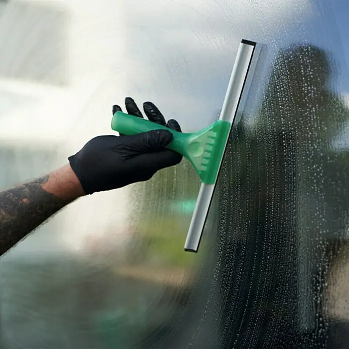 Unger Fenster-Wischer Light - Breite: 30 cm, Kunststoff/Gummi/Aluminium - Fensterreinigung mit einem grünen Abzieher und einer Hand mit schwarzem Handschuh, um streifenfreie Sauberkeit zu erzielen.