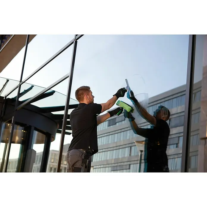 Unger ErgoTec Fenster-Einwascher Ninja - Breite: 45 cm - Ein Fensterputzer reinigt mit einem Abzieher und einem Schwamm eine große Glasfassade. Das Glas spiegelt die Umgebung wider.