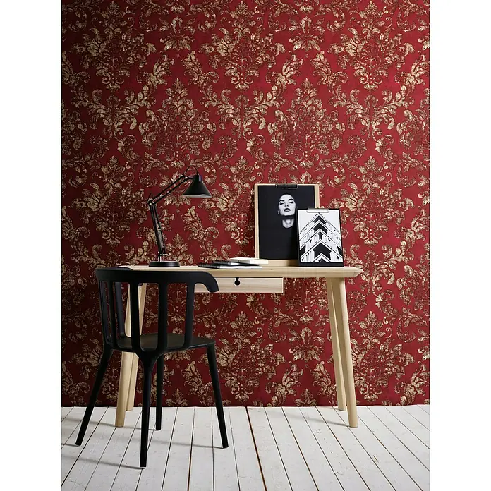 A.S. Création Neue Bude 2.0 ED II Vliestapete Damask - Rot/Gold, Ornament, 10,05 x 0,53 m - Schreibtisch mit Lampe und Dekoration vor einer Wand mit roter und goldener Tapete. Eine schwarze Stuhl steht davor.