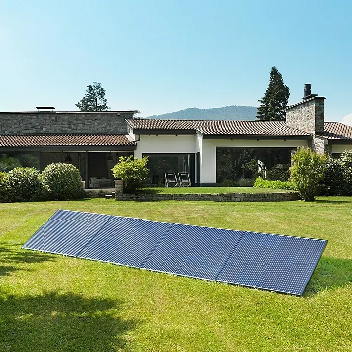 Avidsen Panel solar Soria - L x An x Al: 25 x 760 x 680 mm - Un panel solar azul se encuentra sobre un césped verde frente a una casa moderna, aprovechando la energía solar.