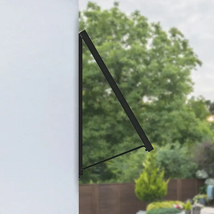 Avidsen Panel solar Soria - L x An x Al: 25 x 760 x 680 mm - Un toldo negro está montado en una pared blanca, proporcionando sombra. Se observan árboles y plantas al fondo.