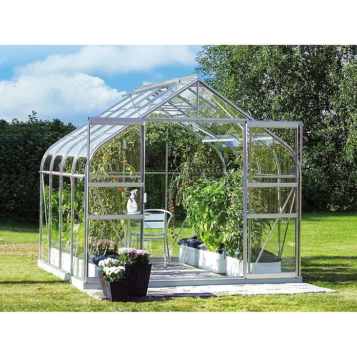 Vitavia Gewächshaus Dione 6700 - Außenmaß inkl. Dachüberstand (B x T): 263,5 x 258 cm, 3 mm, Aluminium - Ein Gewächshaus aus Glas und Metall, gefüllt mit Tomatenpflanzen und Blumen, steht auf einer grünen Wiese unter blauem Himmel.