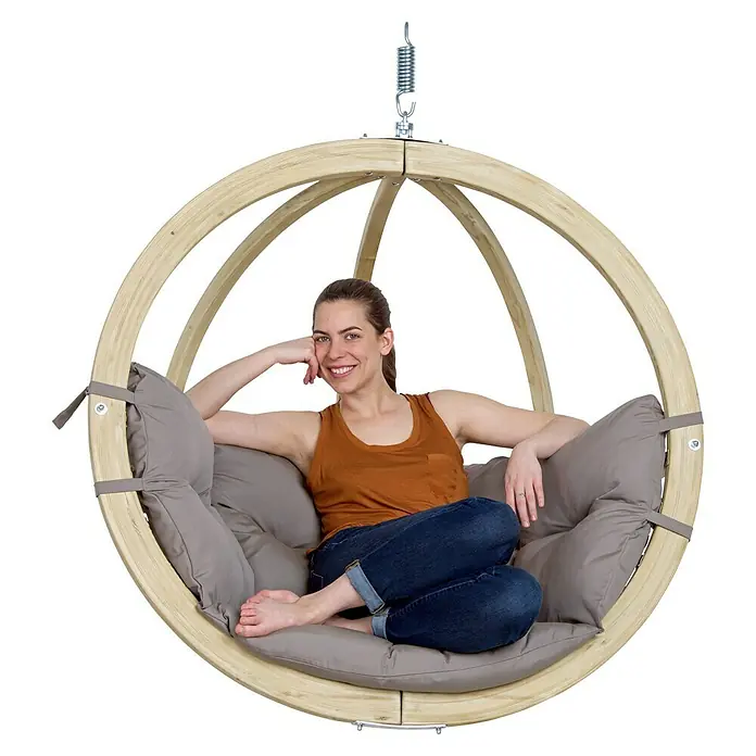 Amazonas Hängesessel Globo Chair - L x B x H: 69 x 118 x 121 cm, Natur/Taupe - Frau sitzt in einem hölzernen Kugel-Hängesessel mit grauen Kissen. Perfekt zum Entspannen im Garten oder auf der Terrasse.