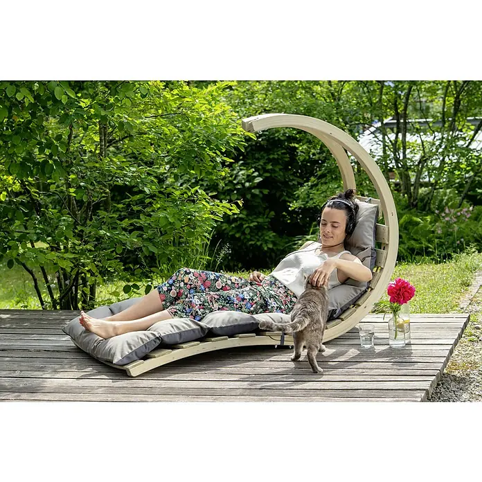 Amazonas Hängeliege Swing Lounger - L x B x H: 240 x 75 x 114 cm, Anthrazit - Eine Frau entspannt auf einer Hängeliege im Garten, während eine Katze sie berührt. Die Liege ist aus Holz und hat bequeme Kissen.