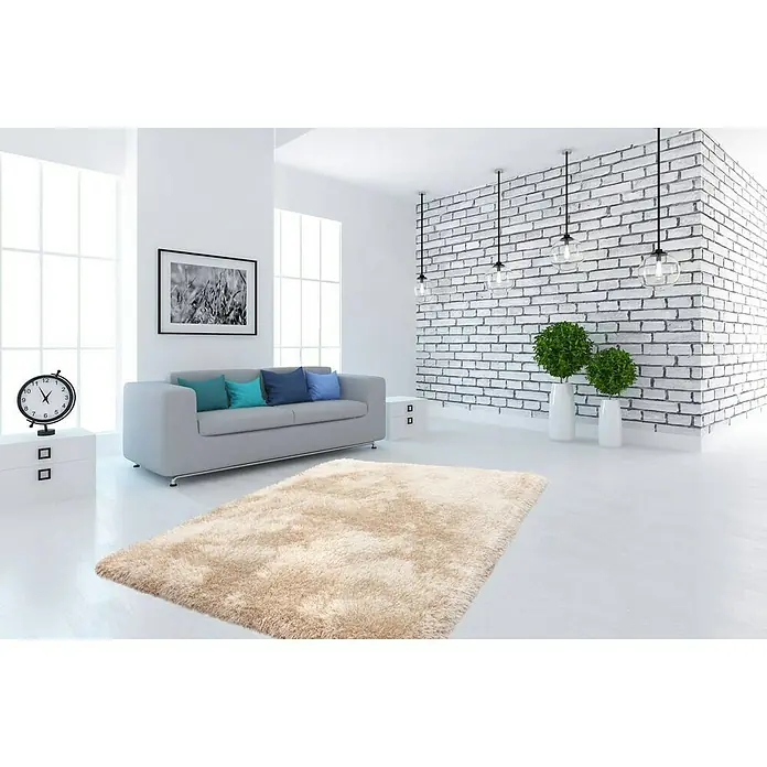 Kayoom Hochflorteppich Cosy - Champagner, 170 x 120 cm, 100 % Polyester - Ein hellbrauner, rechteckiger Zottelteppich liegt in einem hellen, modernen Wohnzimmer. Der Teppich ist weich und flauschig und verleiht dem Raum Wärme.