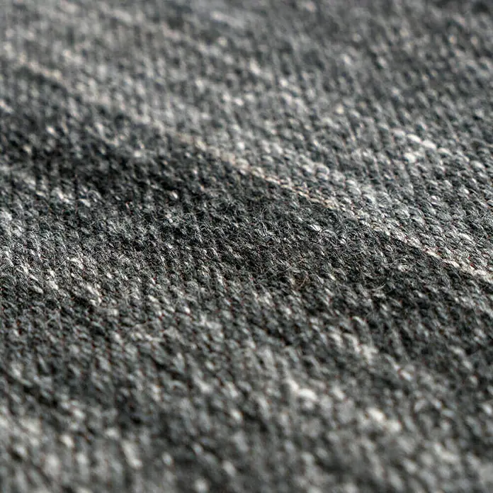 Kayoom Flachgewebeteppich Phönix - Anthrazit, 290 x 200 cm, 75 % Wolle, 20 % Baumwolle, 5 % Polyester - Nahaufnahme eines melierten, grauen Tweed-Stoffs, der die Textur und das Muster des Materials hervorhebt. Perfekt für warme Bekleidung.