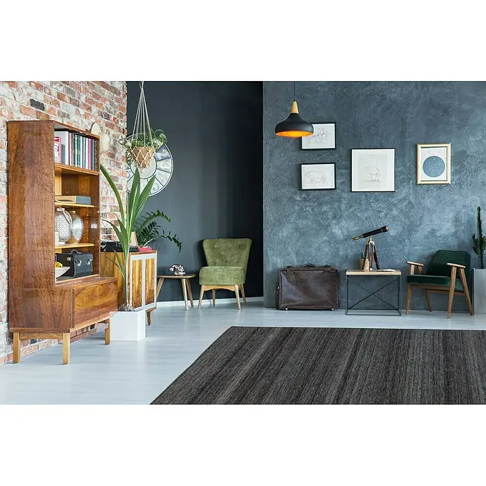 Kayoom Flachgewebeteppich Phönix - Anthrazit, 290 x 200 cm, 75 % Wolle, 20 % Baumwolle, 5 % Polyester - Einrichtung mit einem grauen Teppich, einem Holzbücherregal und grünen Sesseln, die eine gemütliche und stilvolle Atmosphäre schaffen.