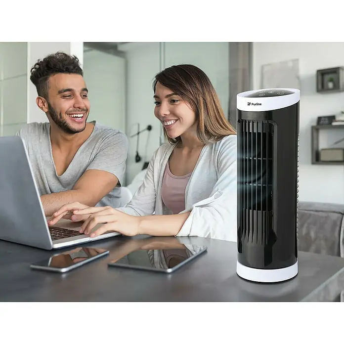 Purline Venty Ventilador de torre Erebus - Negro/Blanco, 33 cm - Un elegante ventilador de torre Purline negro sobre una mesa, con una pareja trabajando en un portátil al fondo.