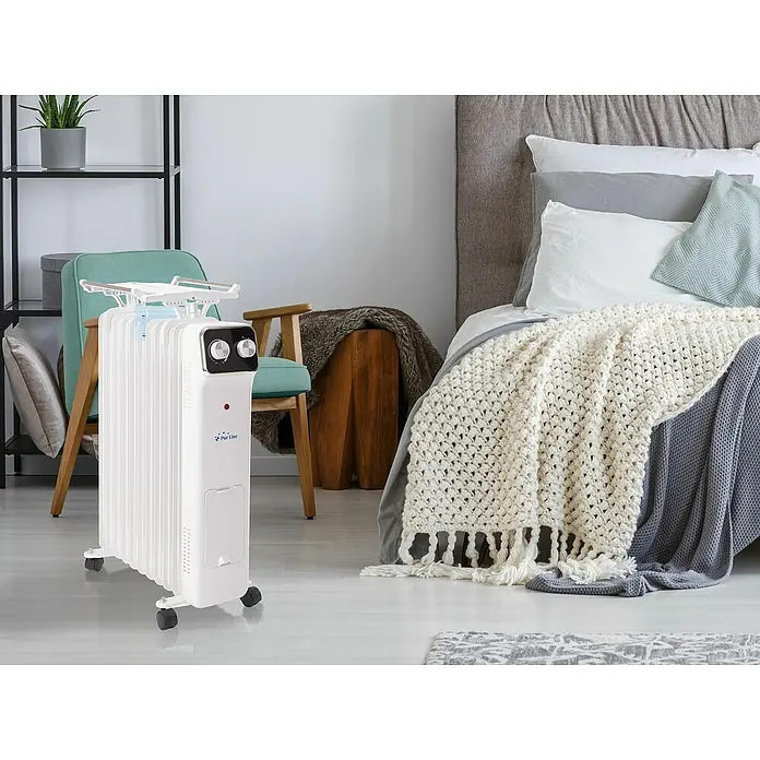Purline Radiador de aceite HOTI OR2000 - 2.000 W, Blanco, 14,5 x 38,5 x 61,5 cm - La imagen muestra un radiador de aceite Purline con tendedero en un dormitorio. Es blanco y tiene un panel de control con botones en la parte superior.