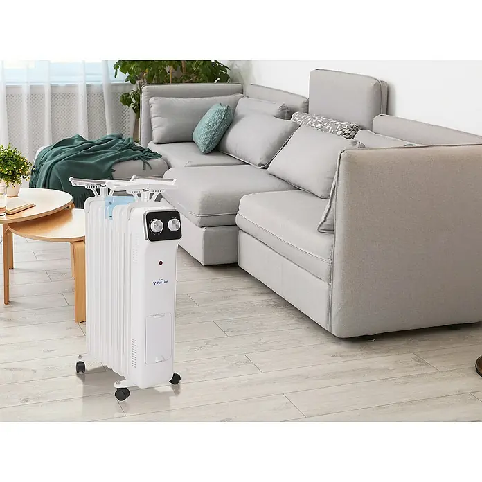 Purline Radiador de aceite HOTI OR2000 - 2.000 W, Blanco, 14,5 x 38,5 x 61,5 cm - Un radiador de aceite Pur Line blanco y portátil se encuentra en la sala de estar con un sofá gris y una mesa de madera. Tiene ruedas y controles.