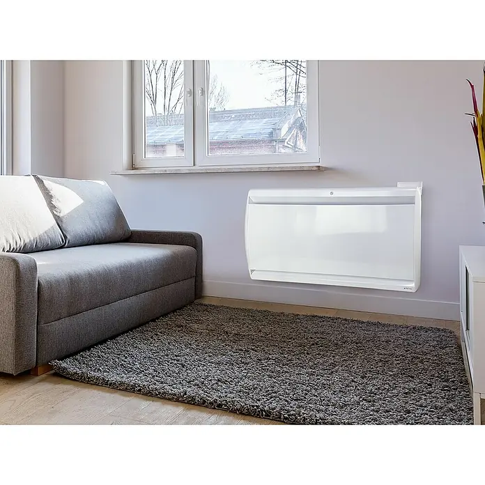 Purline Emisor térmico Micairon A2000 WiFi - 2.000 W, Blanco, 10 x 90 x 55 cm - Un radiador de convección blanco montado en la pared en una sala de estar, con sofá y alfombra grises.