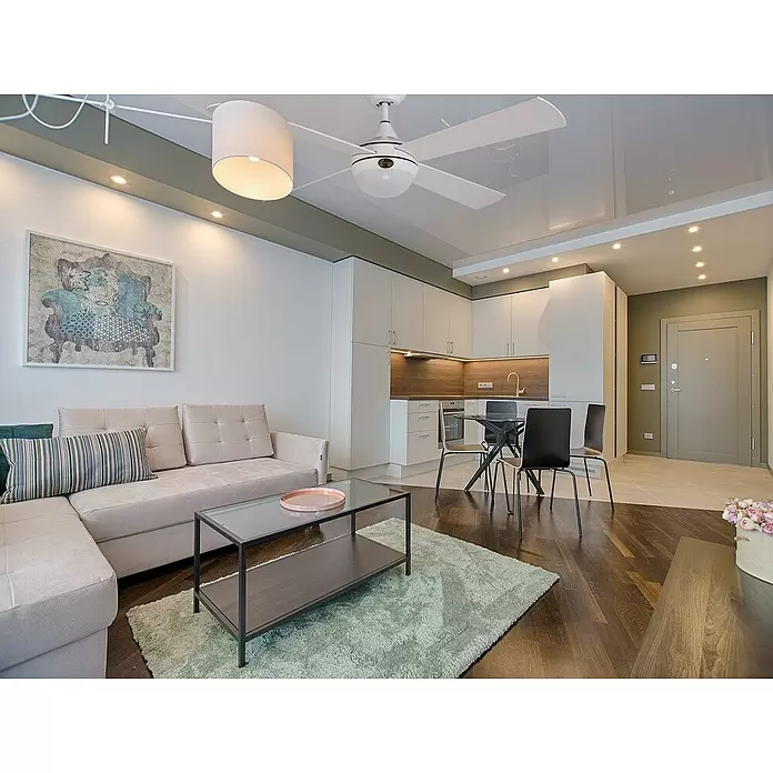 Purline Ventilador de techo Raica - Blanco, 122 cm, 20 W - Sala de estar moderna de planta abierta con un sofá seccional beige, mesa de centro de cristal y cocina blanca integrada.