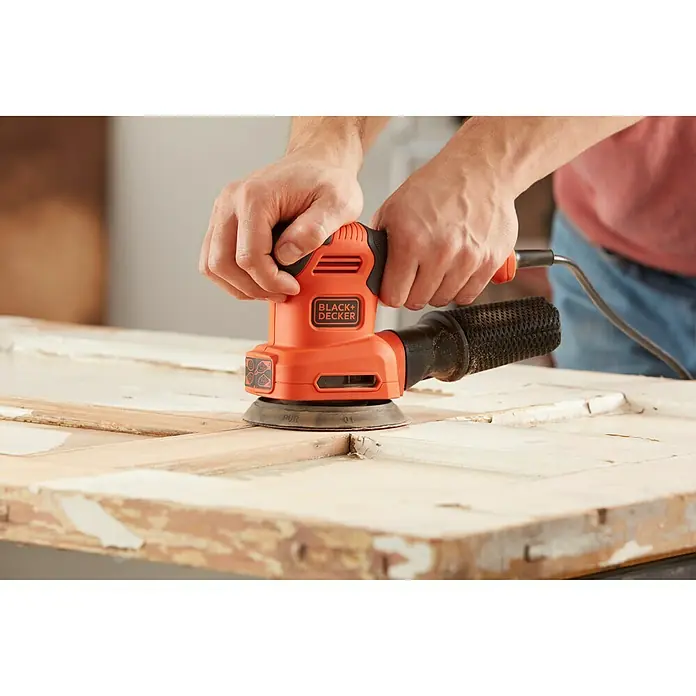 Black+Decker Lijadora multifunción eléctrica  BEW200-QS - 200 W, Número de oscilaciones marcha en vacío: 12.000 r.p.m., Diámetro circuito oscilante: 2 mm - Primer plano de una lijadora orbital aleatoria BLACK+DECKER que se utiliza para lijar una superficie de madera.