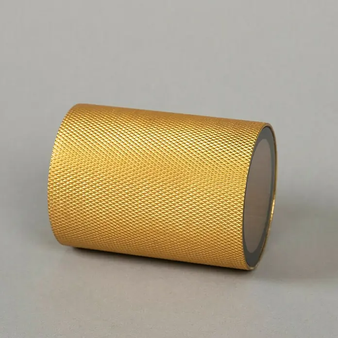 Konstsmide Außenwandleuchte Temi - 7 W, Schwarz/Gold, IP54 - Nahaufnahme eines goldenen, zylinderförmigen Behälters mit strukturierter Oberfläche, ideal für stilvolle Aufbewahrung.