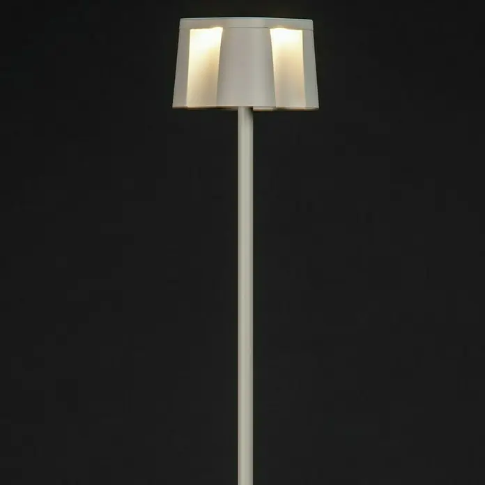 Konstsmide Akku-Stehleuchte Nice - 10 x 10 x 120 cm, Weiß, Mehrfarbig, 3 W, IP54 - Elegante Stehlampe mit weißem Lampenschirm und schlankem, weißen Ständer vor dunklem Hintergrund, die ein warmes Licht ausstrahlt.