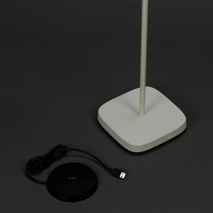 Konstsmide Akku-Stehleuchte Nice - 10 x 10 x 120 cm, Weiß, Mehrfarbig, 3 W, IP54 - Nahaufnahme einer modernen Stehlampe mit quadratischem Sockel und einem Ladegerät, das auf dem Boden liegt.