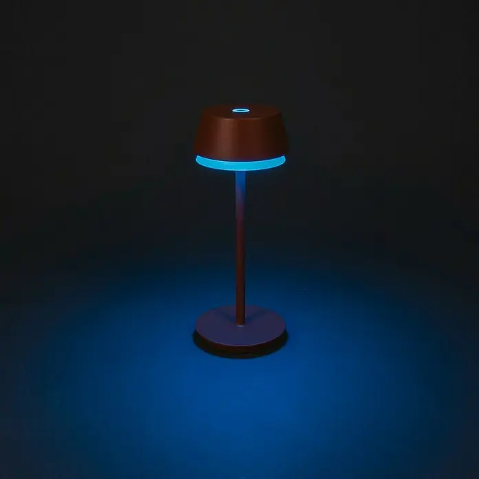 Konstsmide Akku-Tischleuchte Lyon - 2,5 W, L x B x H: 12 x 12 x 30 cm, Braun, RGBW - Nahaufnahme einer modernen Tischleuchte mit braunem Schirm und blauem Licht, die eine stimmungsvolle Atmosphäre erzeugt.