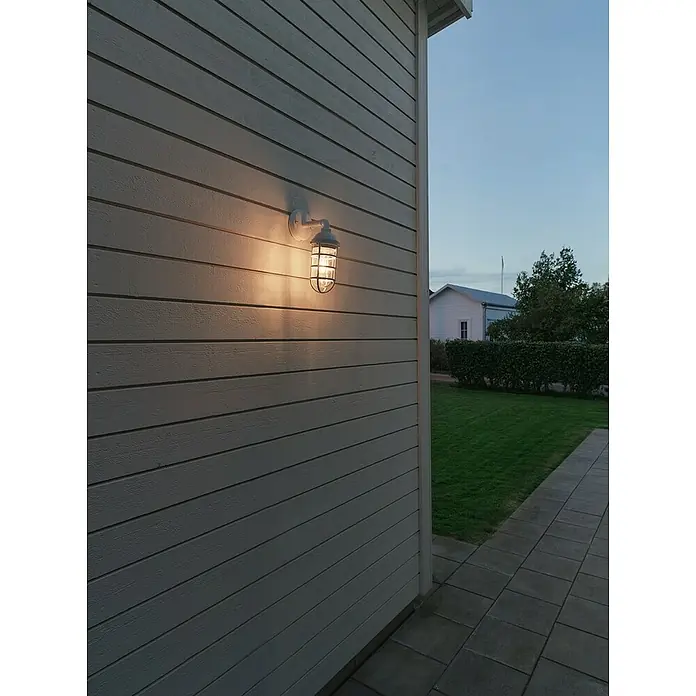 Konstsmide Außenwandleuchte Olbia - 20 W, Weiß, IP44 - Eine Außenwandleuchte mit Käfig, die ein warmes, einladendes Licht auf eine Fassade wirft, ideal für stimmungsvolle Außenbereiche.
