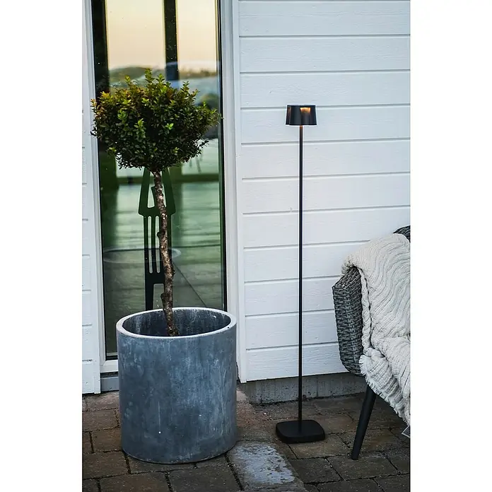 Konstsmide Akku-Stehleuchte Nice - 10 x 10 x 120 cm, Schwarz, Mehrfarbig, 3 W, IP54 - Stilvolle Außenaufnahme mit einer eleganten Stehlampe neben einem Zierbaum im Topf.