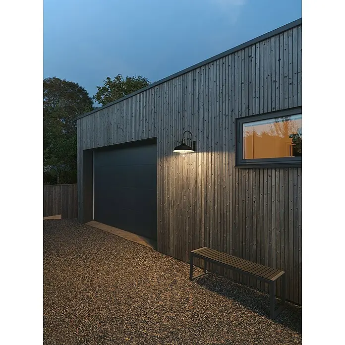 Konstsmide Außenwandleuchte Trapani - 20 W, Schwarz, IP44 - Eine stilvolle Außenwandleuchte beleuchtet eine moderne Garage mit Holzverkleidung und einer Bank davor, die eine einladende Atmosphäre schafft.