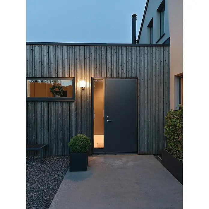 Konstsmide LED-Außenwandleuchte Portici - 20 W, Schwarz, Weiß, IP44 - Außenansicht eines Hauses mit dunkler Holzfassade, moderner Tür und einem Fenster mit Pflanze, beleuchtet durch eine Außenleuchte.