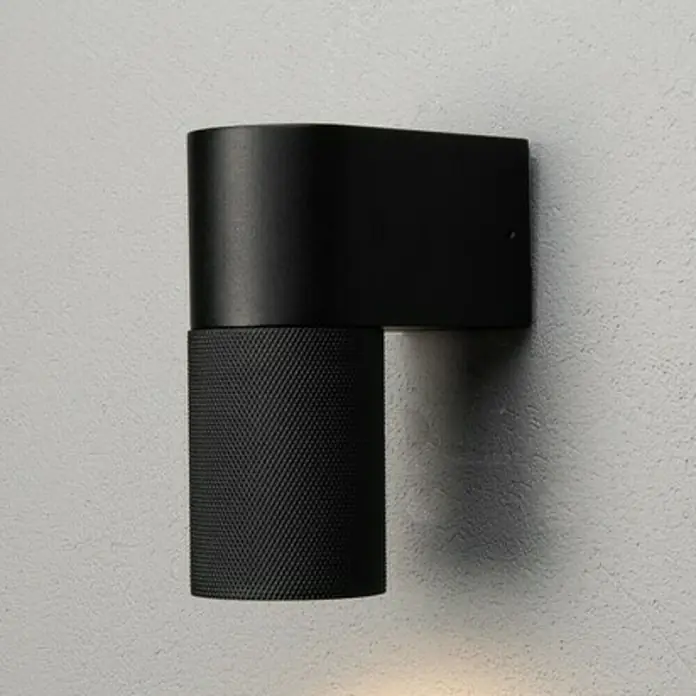 Konstsmide Außenwandleuchte Temi - 7 W, Schwarz, IP54 - Eine moderne, schwarze Wandleuchte mit zylindrischem Schirm und matter Oberfläche, die ein elegantes Licht an die Wand projiziert.