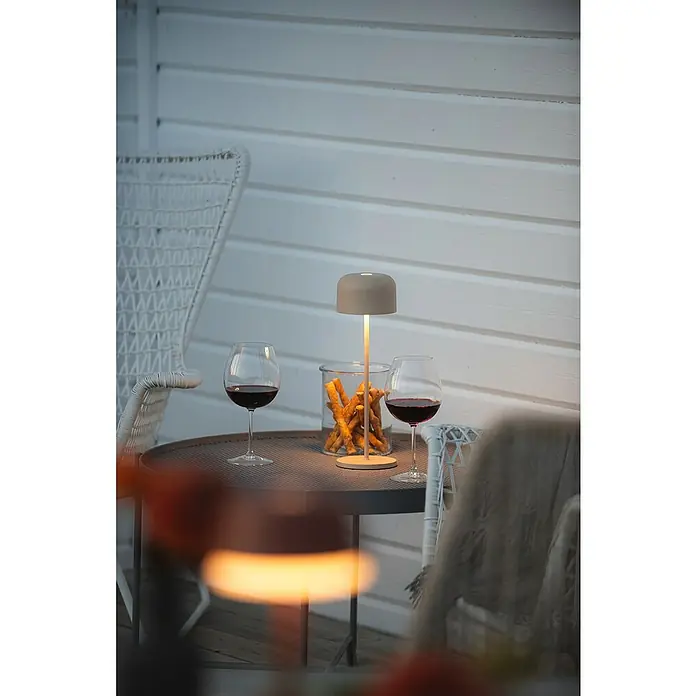 Konstsmide Akku-Tischleuchte Lille - 3,5 W, L x B x H: 11 x 11 x 36 cm, Sand, Mehrfarbig - Elegante Tischleuchte neben Weingläsern und Knabbergebäck auf einem runden Tisch. Das gedämpfte Licht sorgt für eine gemütliche Atmosphäre im Freien.