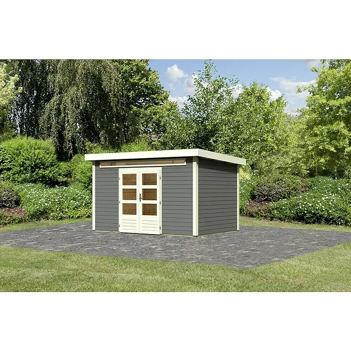 Karibu Gartenhaus Kandern 7 - Außenmaß inkl. Dachüberstand (B x T): 396 x 273 cm, Holz, Terragrau - Ein modernes Gartenhaus mit grauem Holz und hellen Akzenten steht auf einer gepflasterten Fläche, umgeben von üppigem Grün.