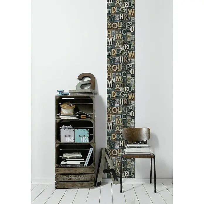 A.S. Création Designpanel pop.up - Buchstaben, Bunt, 35 cm x 2,5 m - Einrichtung mit einem Regal aus Holzkisten, einem Stuhl mit Büchern und einer Wand mit Buchstabenmuster für ein Vintage-Flair.