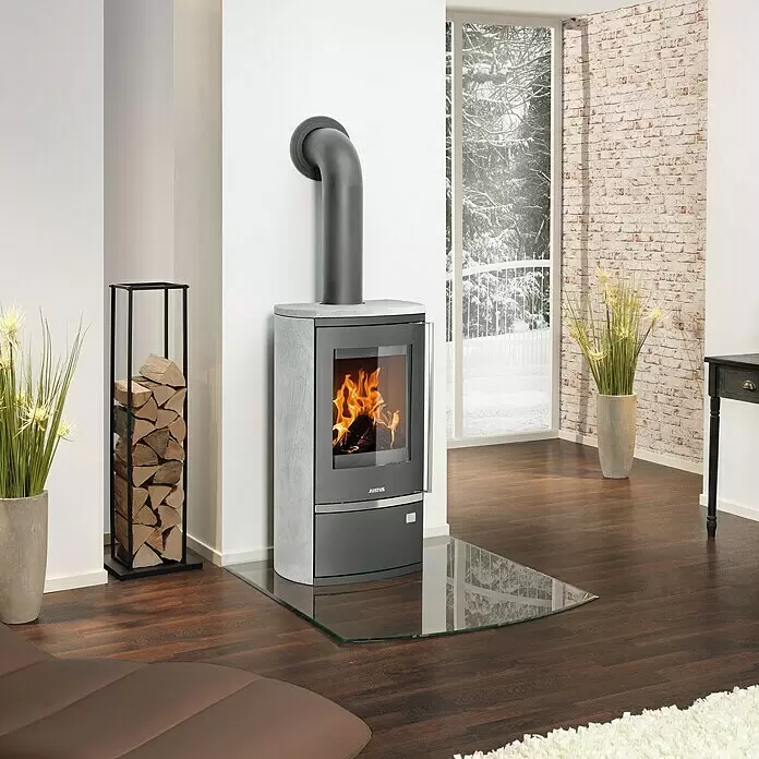Justus Kaminofen Reno R - 6 kW, Raumheizvermögen: 124 m³, Material Verkleidung: Stahl, Schwarz - Grauer Kaminofen mit Glastür, sichtbaren Flammen, auf Glasbodenplatte, neben schwarzem Holzregal.